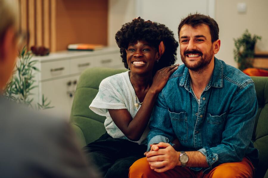 A couple sitting beside each other on a sofa during a therapy session in a sunlit office.