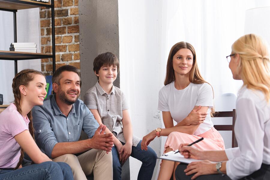 A family sitting together in a sunlit therapy office, listening attentively as the clinician facilitates.