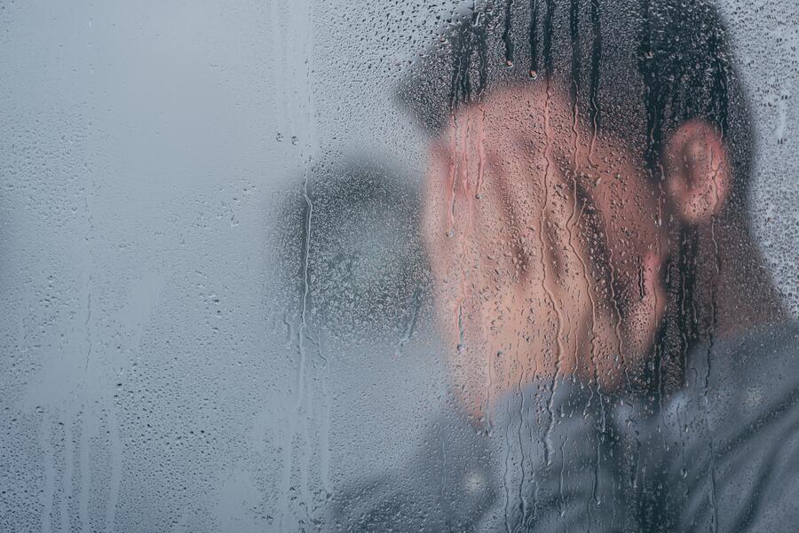 Raindrops on a window beside a person in soft focus, suggesting reflection.